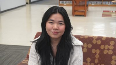 Picture of a girl with long, dark hair and a white zip down jacket sitting on a couch.