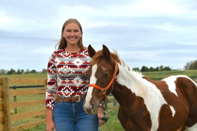 Ashtyn Dunn stands holding a horse's bridle on a farm