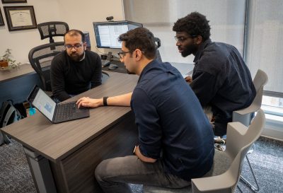 three computer scientists talk around laptop